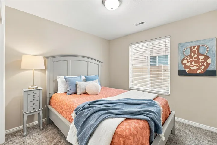 Bright secondary bedroom featuring a curved-top upholstered headboard, carpeted flooring, plantation shutters, recessed ceiling lighting, and a coordinated bedding ensemble with decorative pillows