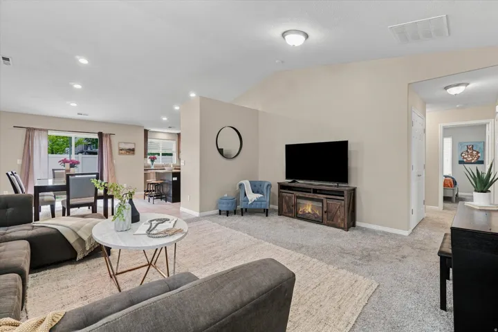 Spacious open-concept living area featuring recessed ceiling lighting, a wood-finish media console with built-in fireplace, neutral carpeting, and large flat-screen television mount