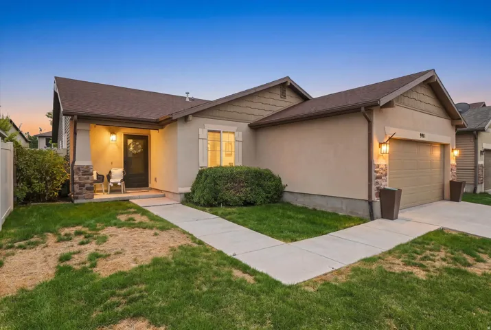 Charming single-story residence featuring a welcoming front porch with warm lighting, neutral stucco exterior, and a two-car garage