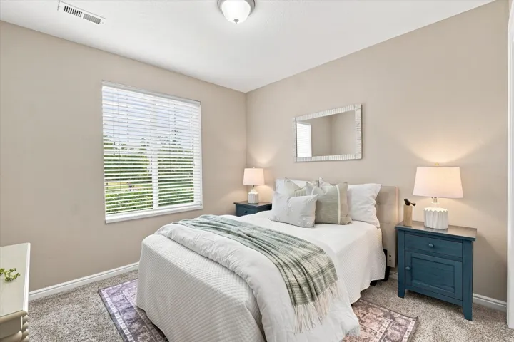 Serene primary bedroom retreat featuring soft neutral walls, abundant natural light from large plantation-shutter windows, dual bedside tables with integrated lighting, and plush bedding with layered textiles