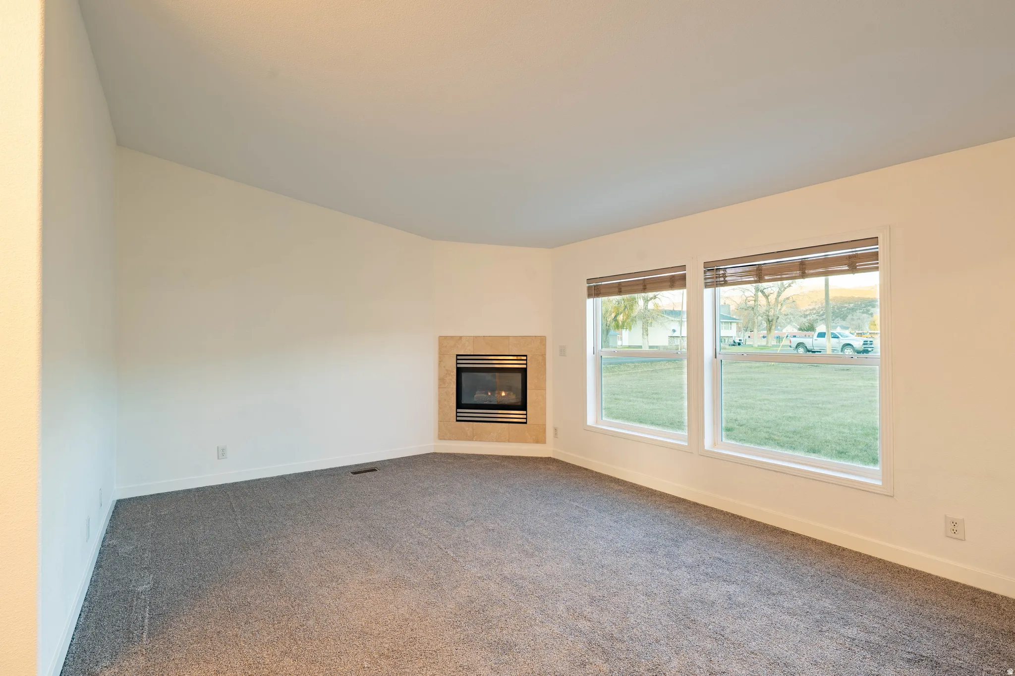 Corner-set fireplace with a stone-finish surround, two large windows, and neutral carpeting