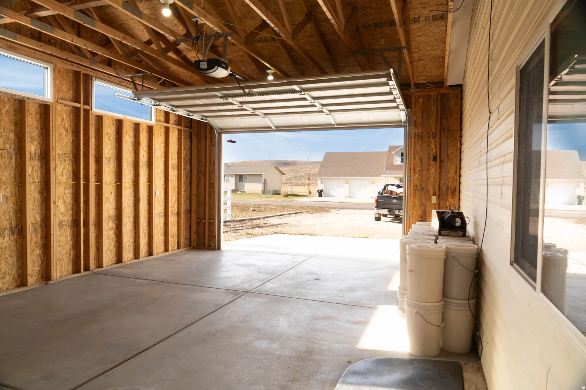 Exposed wood framing, concrete flooring, overhead garage door with opener, and permanent lighting fixtures