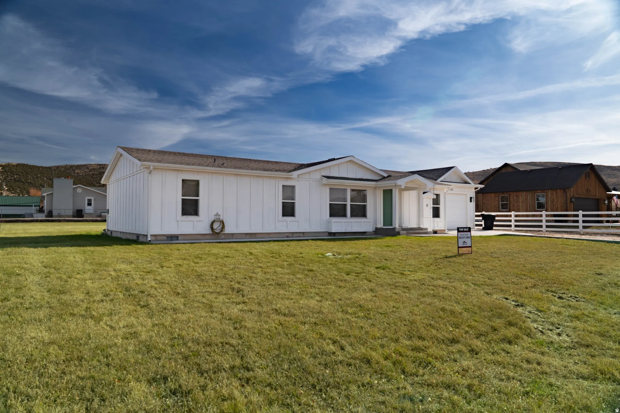 White vertical siding exterior, attached two-car garage, covered porch entry, white picket fence, and a spacious grassy yard