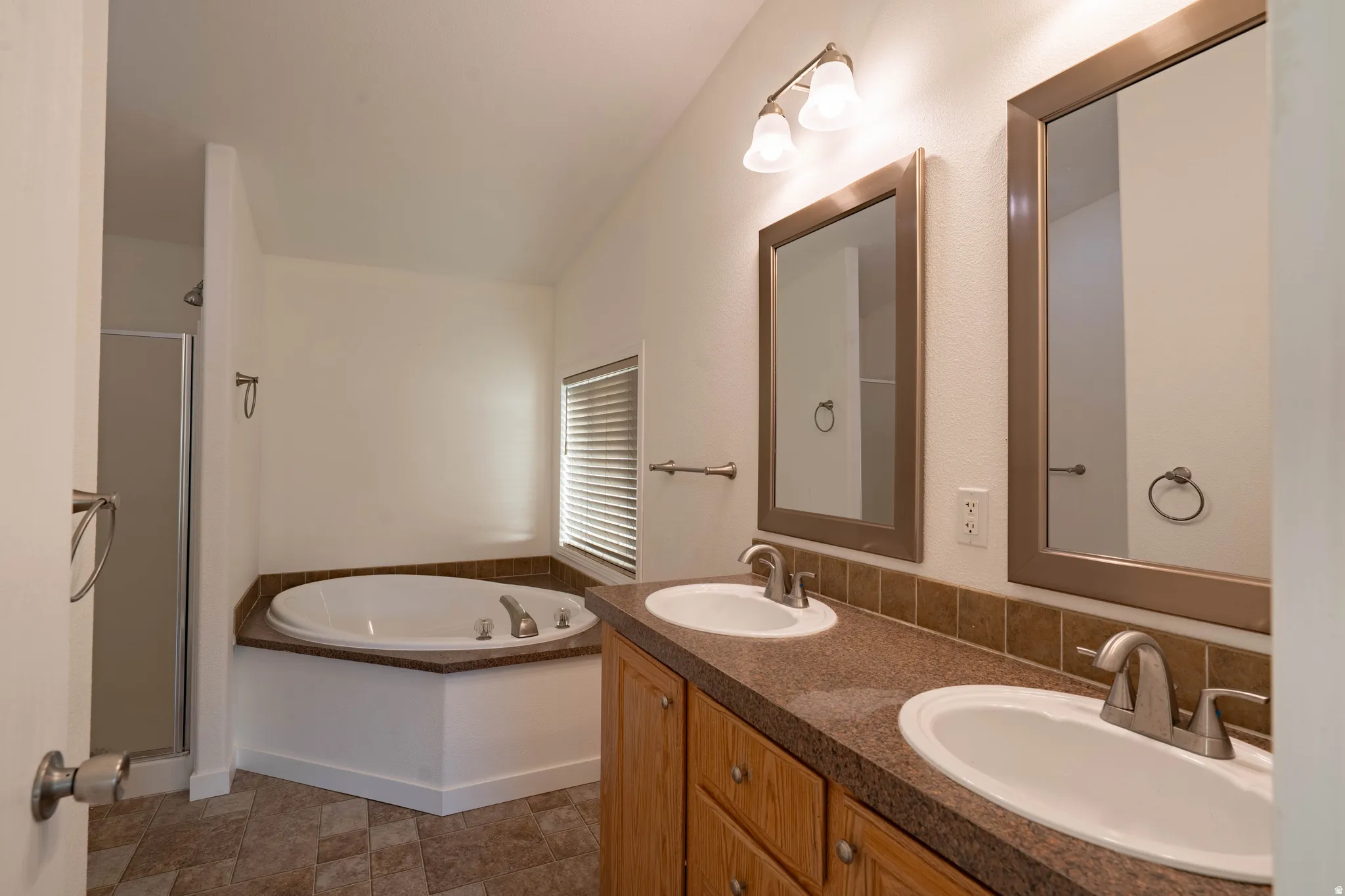 Dual vanity with integrated sinks, framed mirrors, corner soaking tub, and a separate shower enclosure