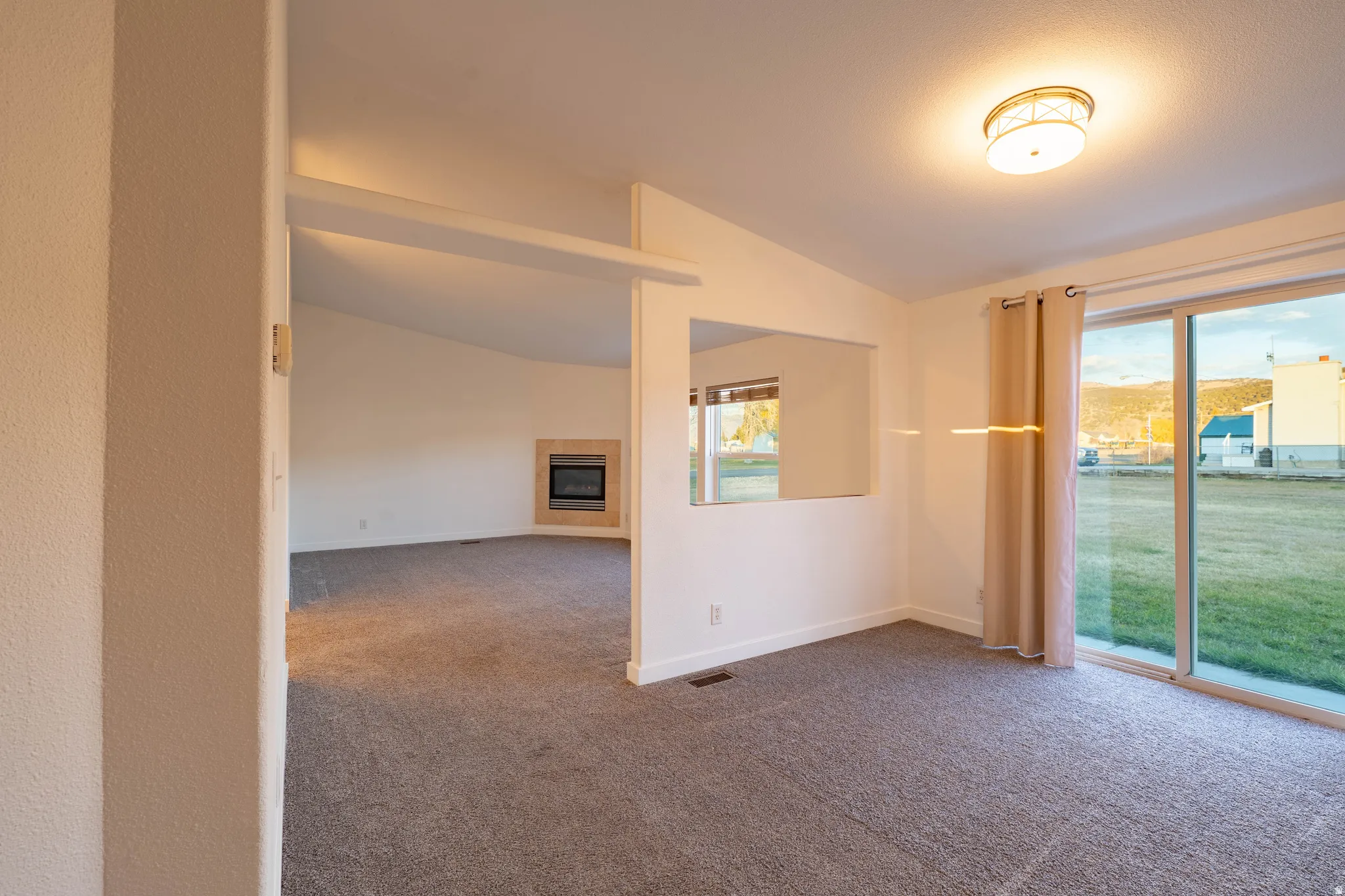 Sliding glass door, wall-mounted mirror, recessed fireplace, vaulted ceiling, and flush-mount ceiling light