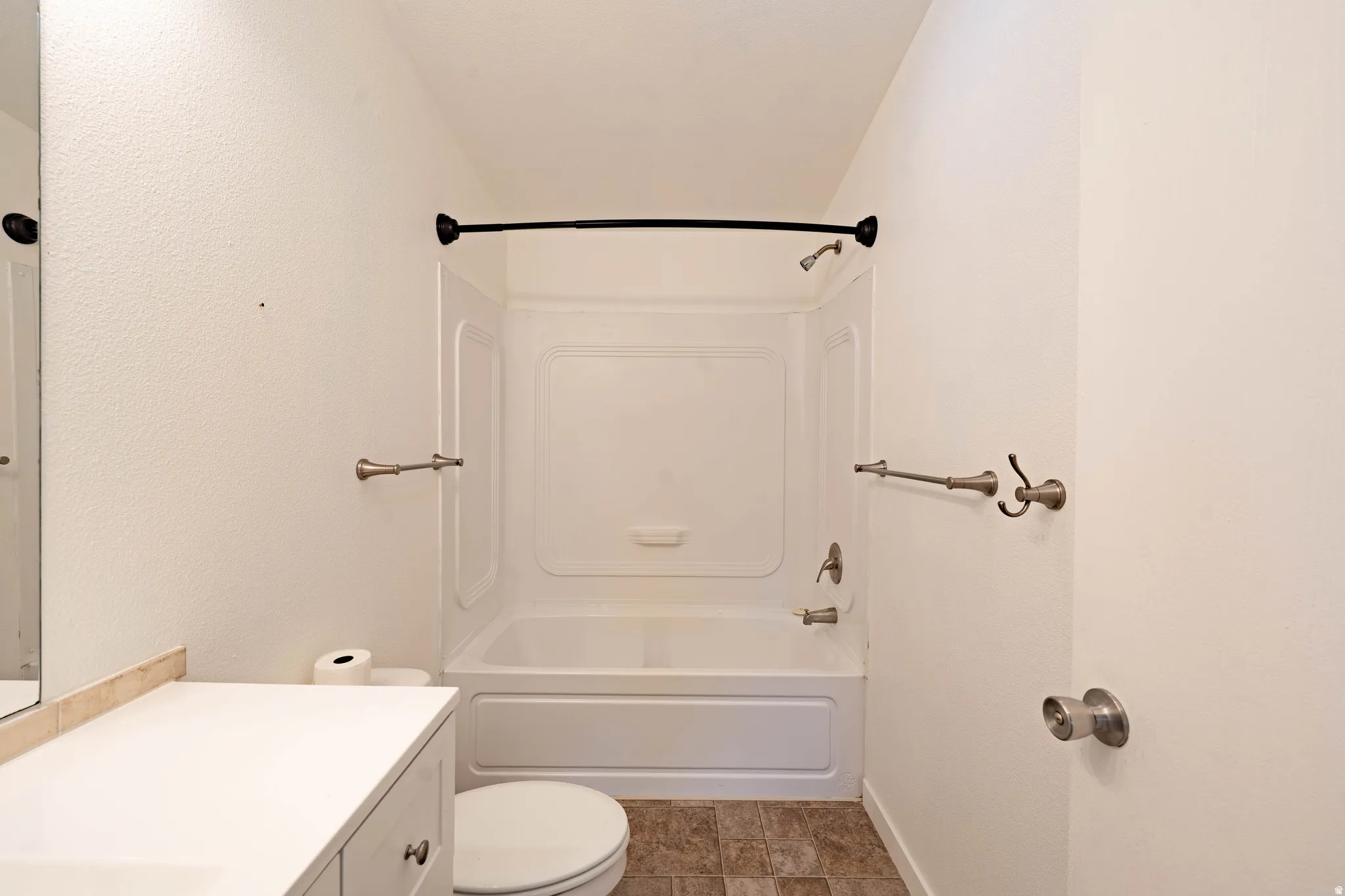 White vanity with a neutral countertop, white toilet, white tub with shower, and tile flooring