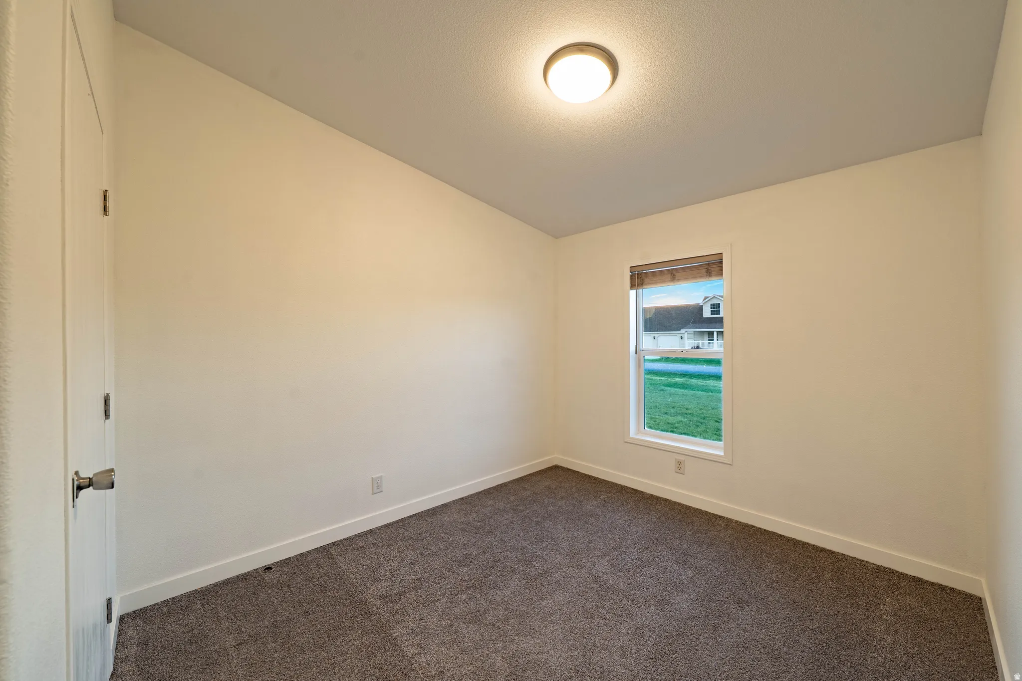 Neutral wall color with a single window, overhead lighting, and carpeted flooring