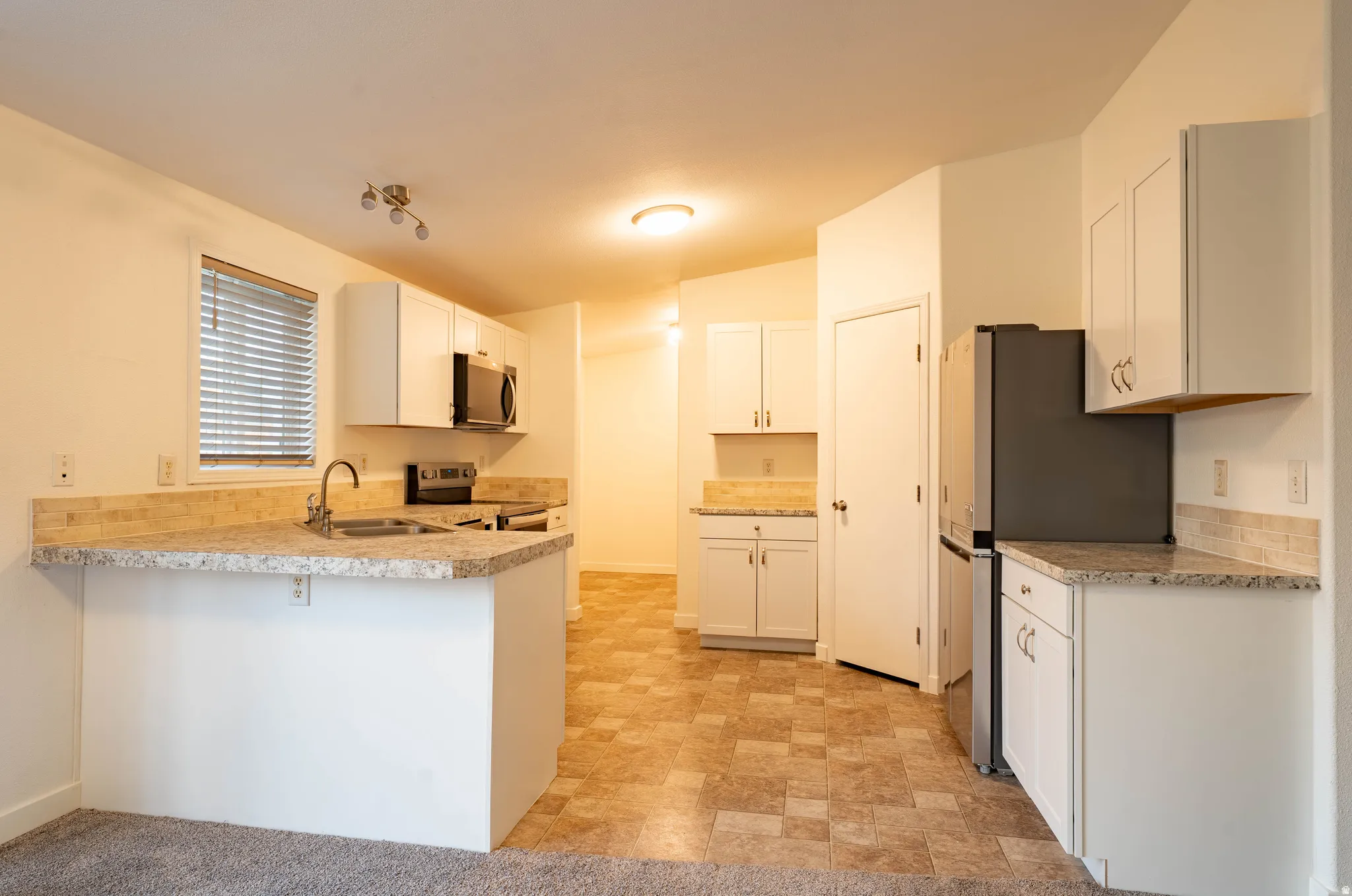 Kitchen featuring white cabinetry, light-toned countertops, stainless steel appliances, and a tiled backsplash