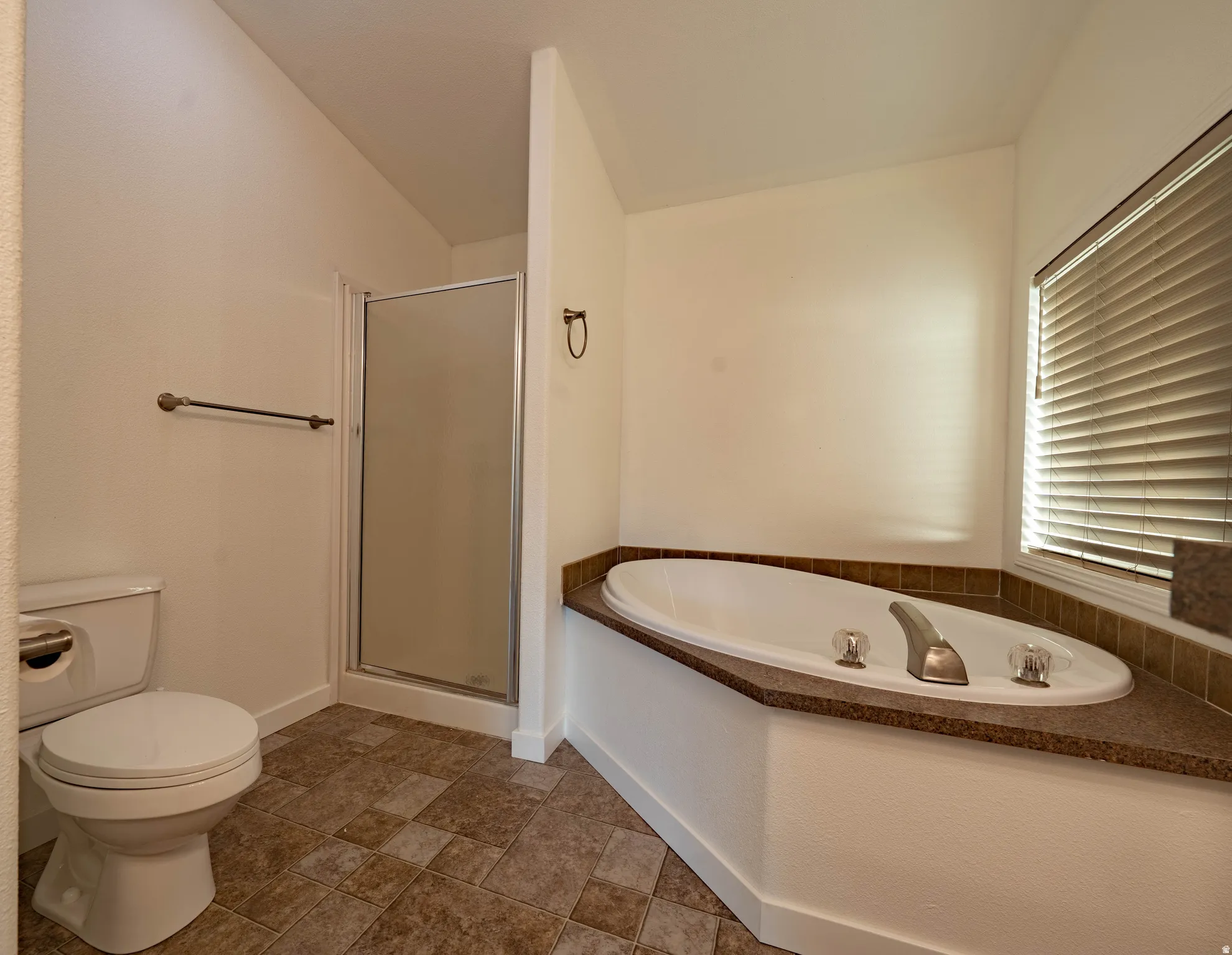 Corner soaking tub with textured countertop, glass-enclosed shower, and varied tile flooring