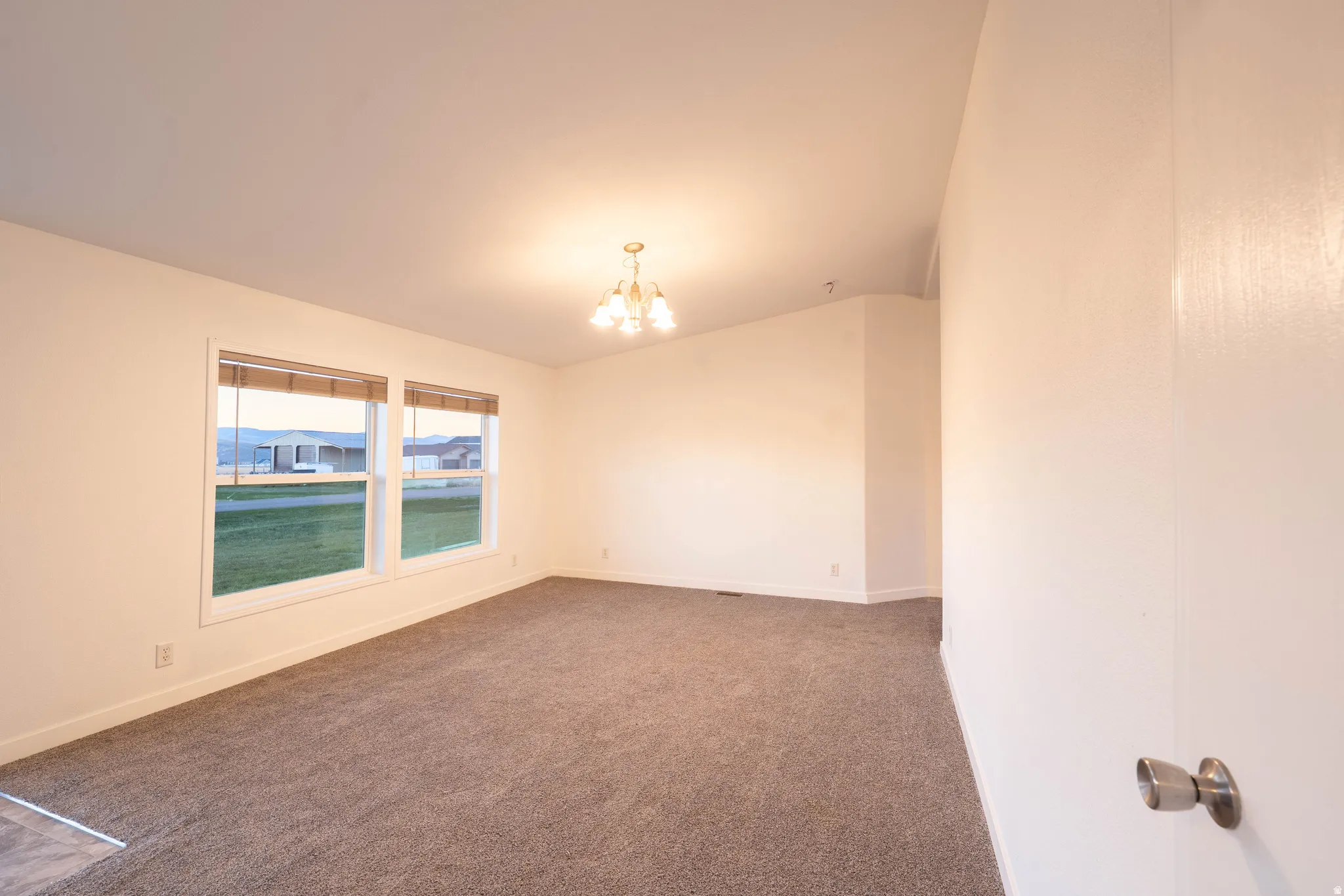 Neutral-toned carpeting, dual windows with blinds, and an overhead chandelier light fixture