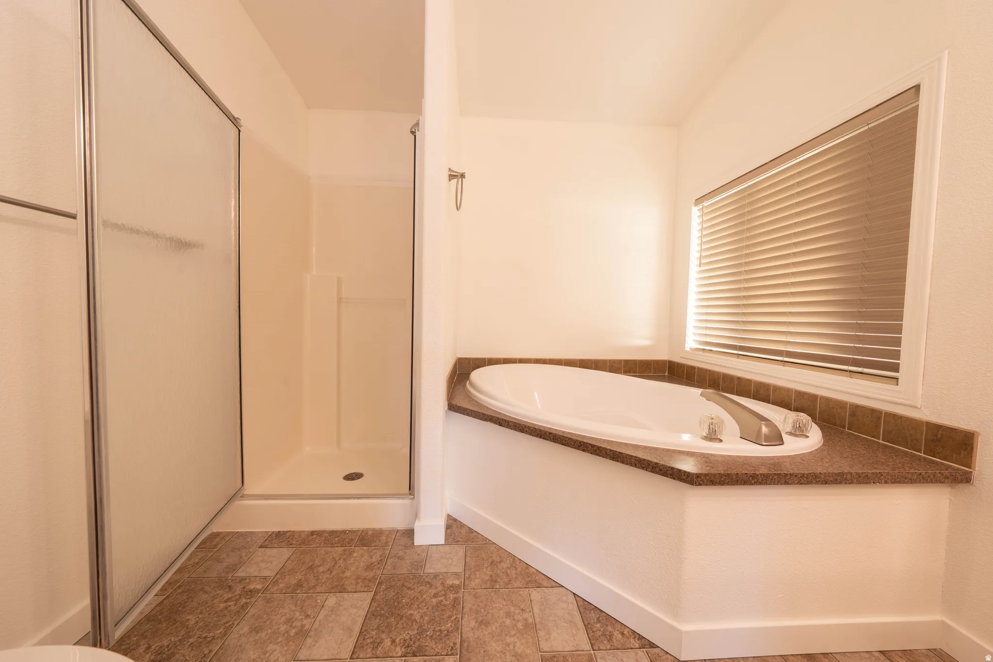 Corner soaking tub with a tiled surround, adjacent to a separate shower enclosure with a frosted glass door, and tiled flooring