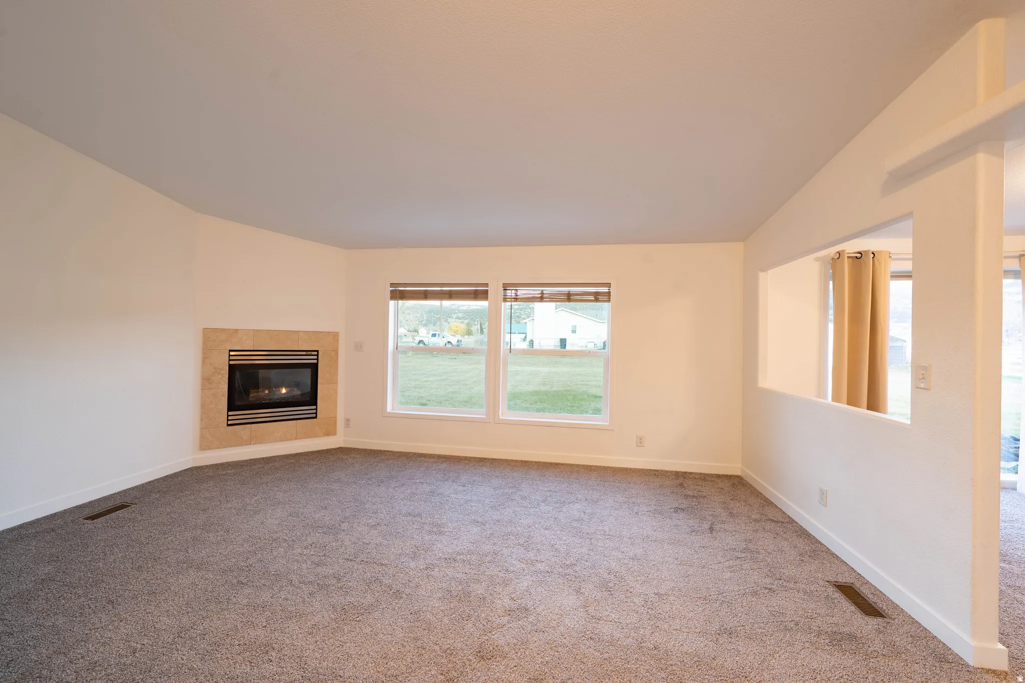 Recessed fireplace with a stone surround, large windows with blinds, and neutral carpeting