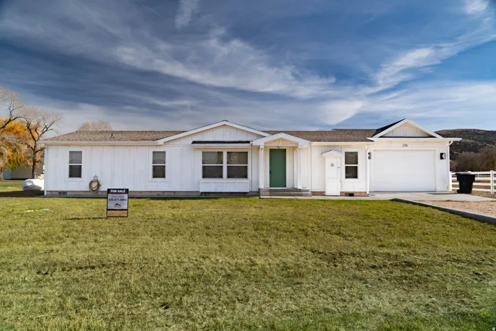 White siding exterior, attached garage, green entry door, concrete driveway, and white fencing