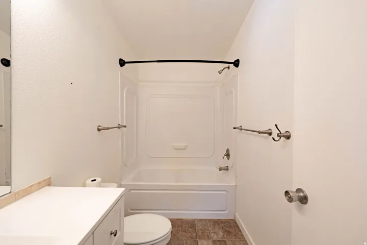 White vanity with a neutral countertop, white toilet, white tub with shower, and tile flooring