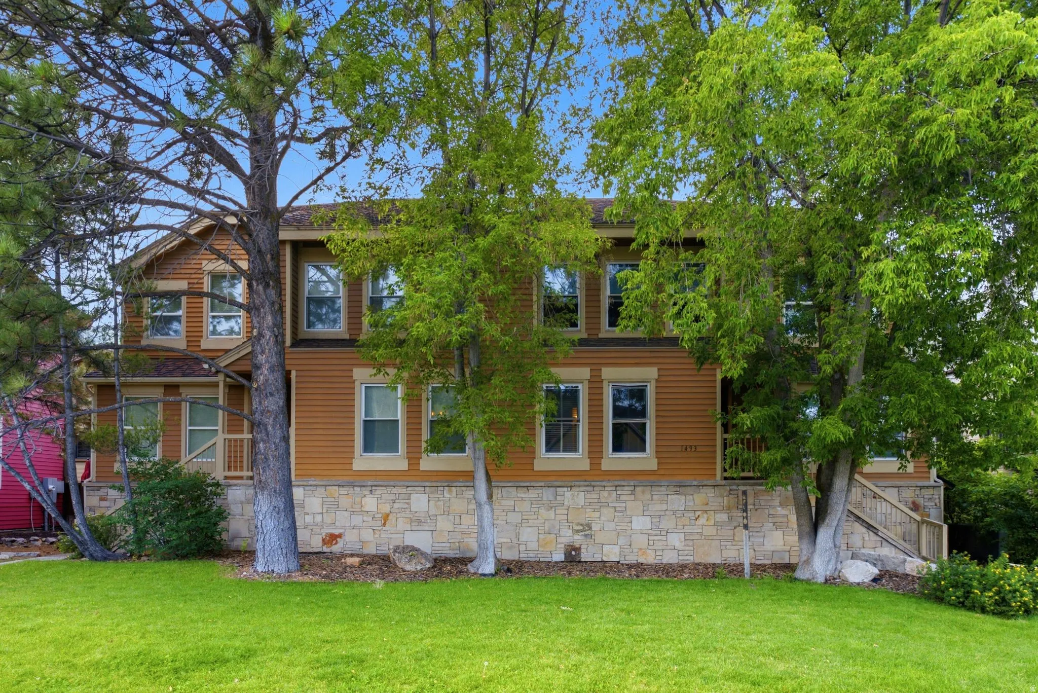 Two-story residence featuring horizontal siding and stone veneer, multiple windows with white trim, and a prominent front lawn with mature trees