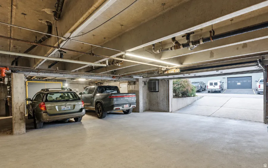 Underground parking garage featuring concrete flooring, exposed overhead piping, and fluorescent strip lighting