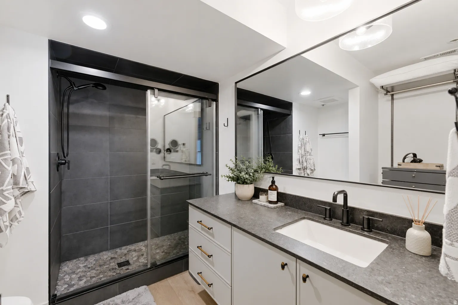Glass-enclosed shower with dark gray tile surround and pebble-finish floor