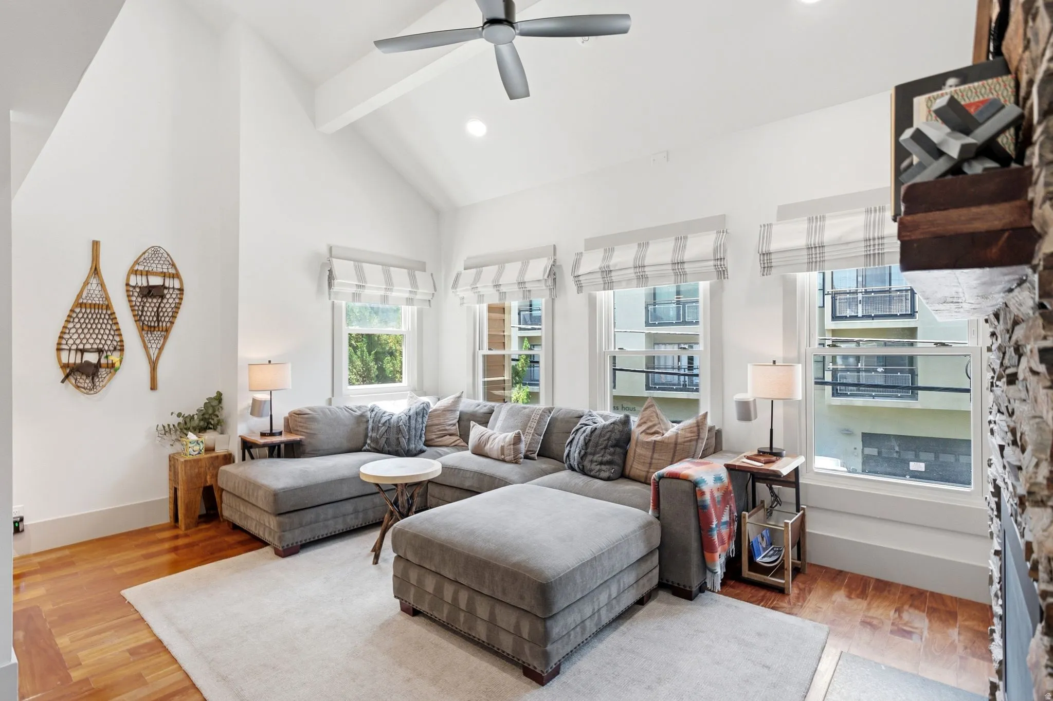 Vaulted ceiling with exposed beam, wood-finish flooring, recessed lighting, ceiling fan, and multiple windows with window treatments