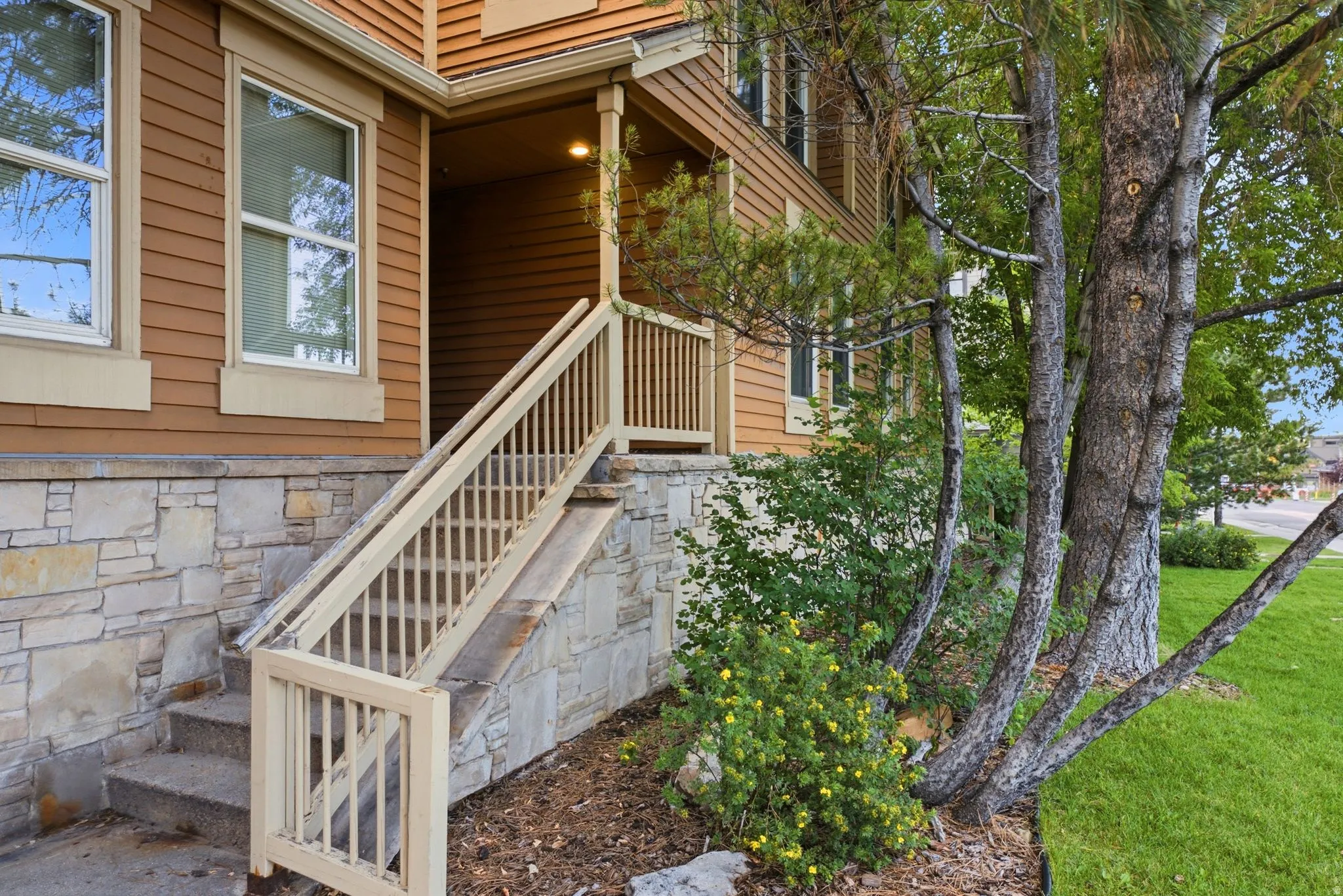 Stone veneer foundation with steps and a porch featuring a wood railing