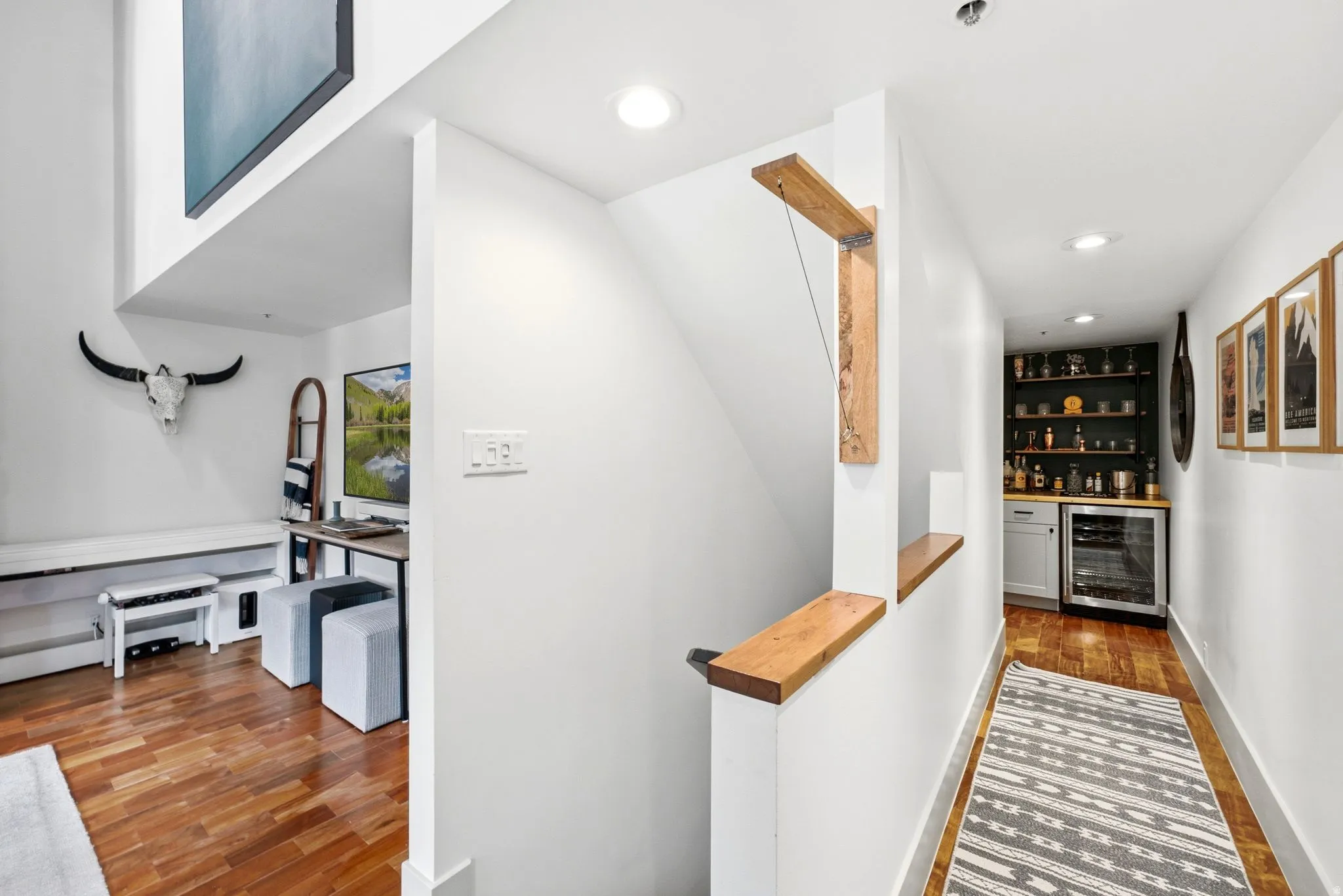 Wood-finish flooring throughout, built-in shelving, recessed lighting, integrated beverage cooler, and a custom wood staircase