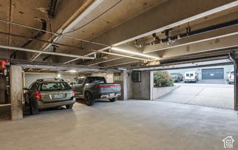Underground parking garage featuring concrete flooring, exposed overhead piping, and fluorescent strip lighting