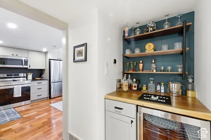 Custom built-in bar with wood-finish countertop, open shelving, and integrated beverage cooler