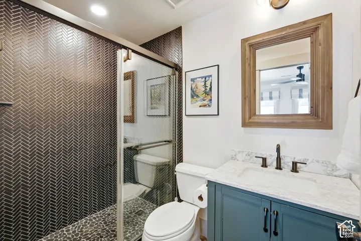 Herringbone-patterned shower tiling, pebble shower floor, glass shower enclosure, wood-framed mirror, and a vanity with a stone-finish countertop