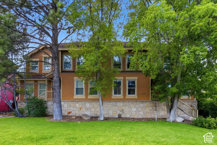 Two-story residence featuring horizontal siding and stone veneer, multiple windows with white trim, and a prominent front lawn with mature trees
