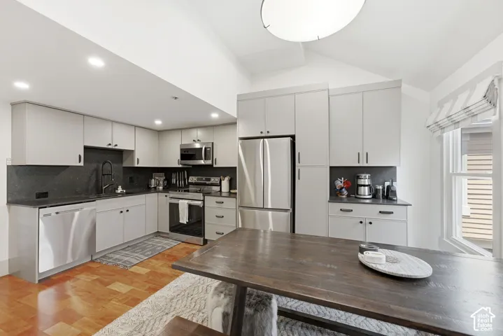 Modern kitchen featuring light gray cabinetry, stainless steel appliances, dark countertops with a coordinating backsplash, and wood-finish flooring