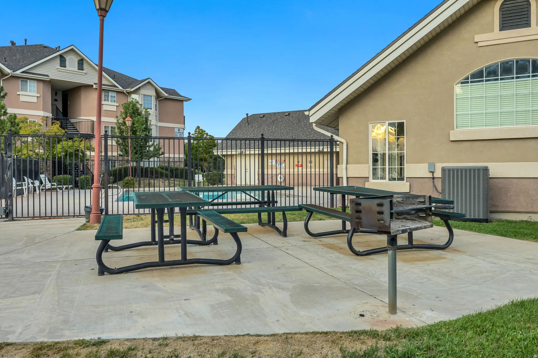Concrete patio area featuring two picnic tables, a built-in barbecue grill, and a black wrought iron fence
