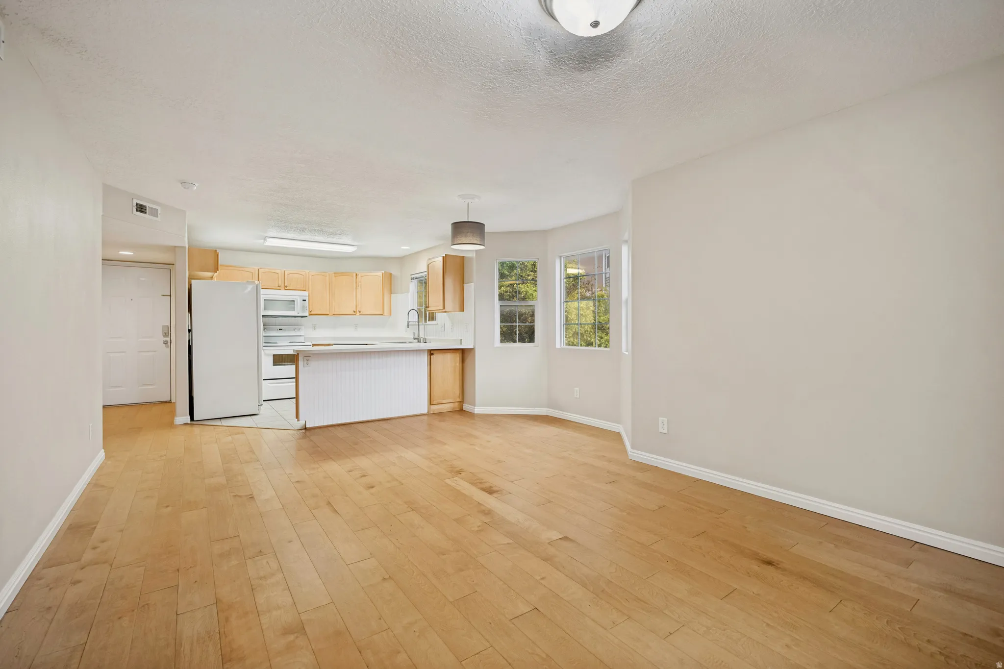 Open-concept living area with wood-finish flooring, recessed lighting, and a kitchen featuring wood cabinetry and white appliances