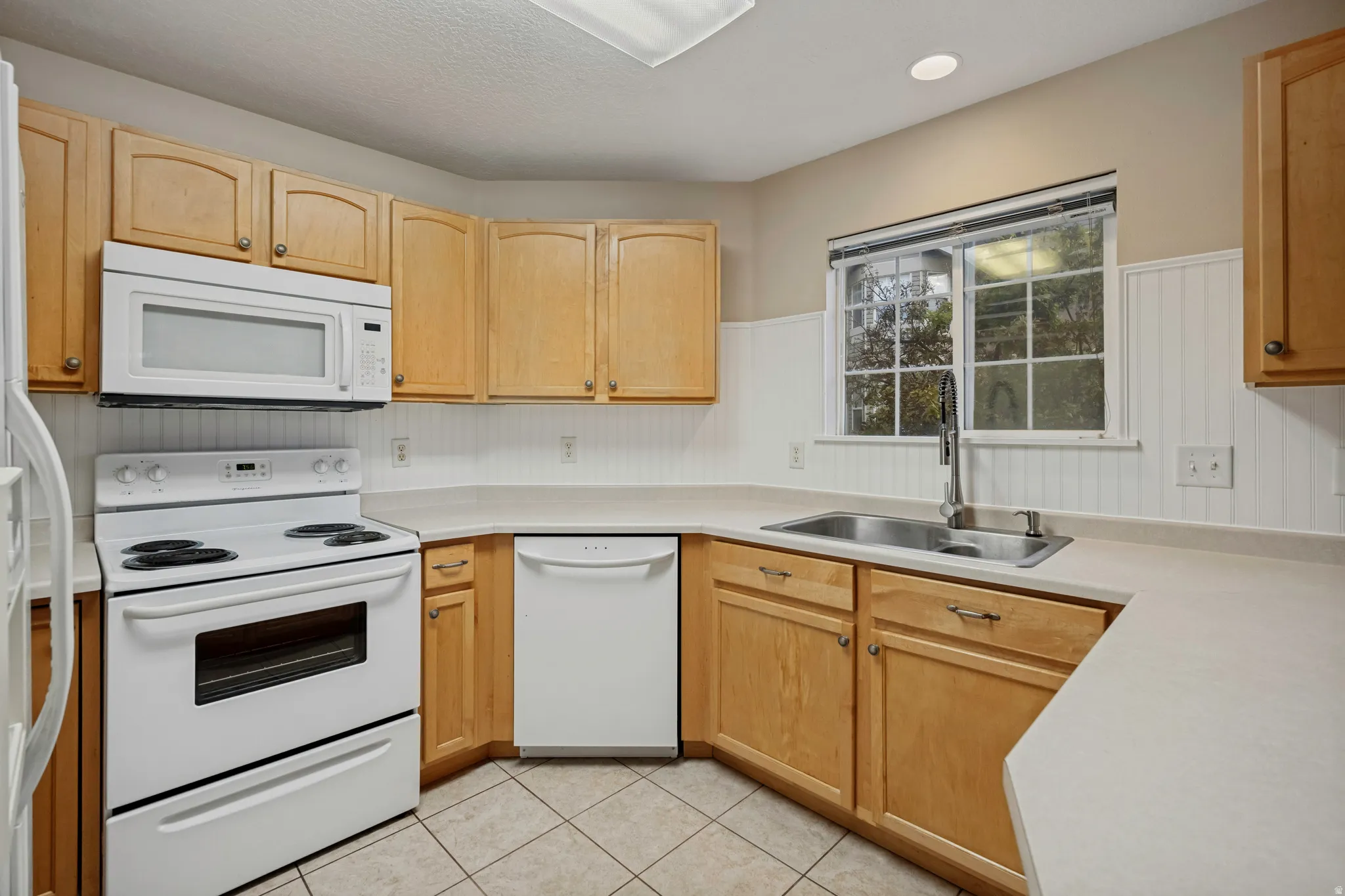 Kitchen featuring wood cabinetry, white appliances, solid surface countertops, and tile flooring