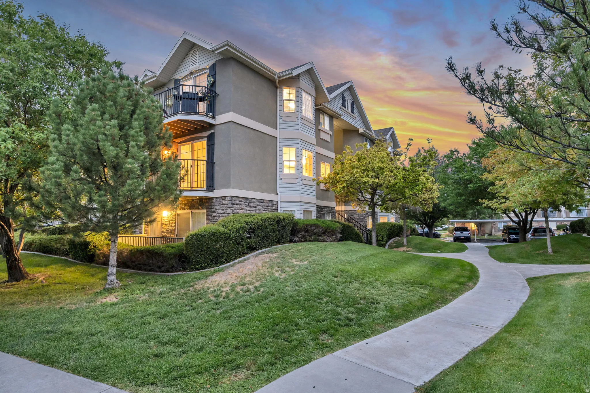 Multi-story residence featuring balconies with wrought iron railings, stone detailing on the lower facade, and mature landscaping