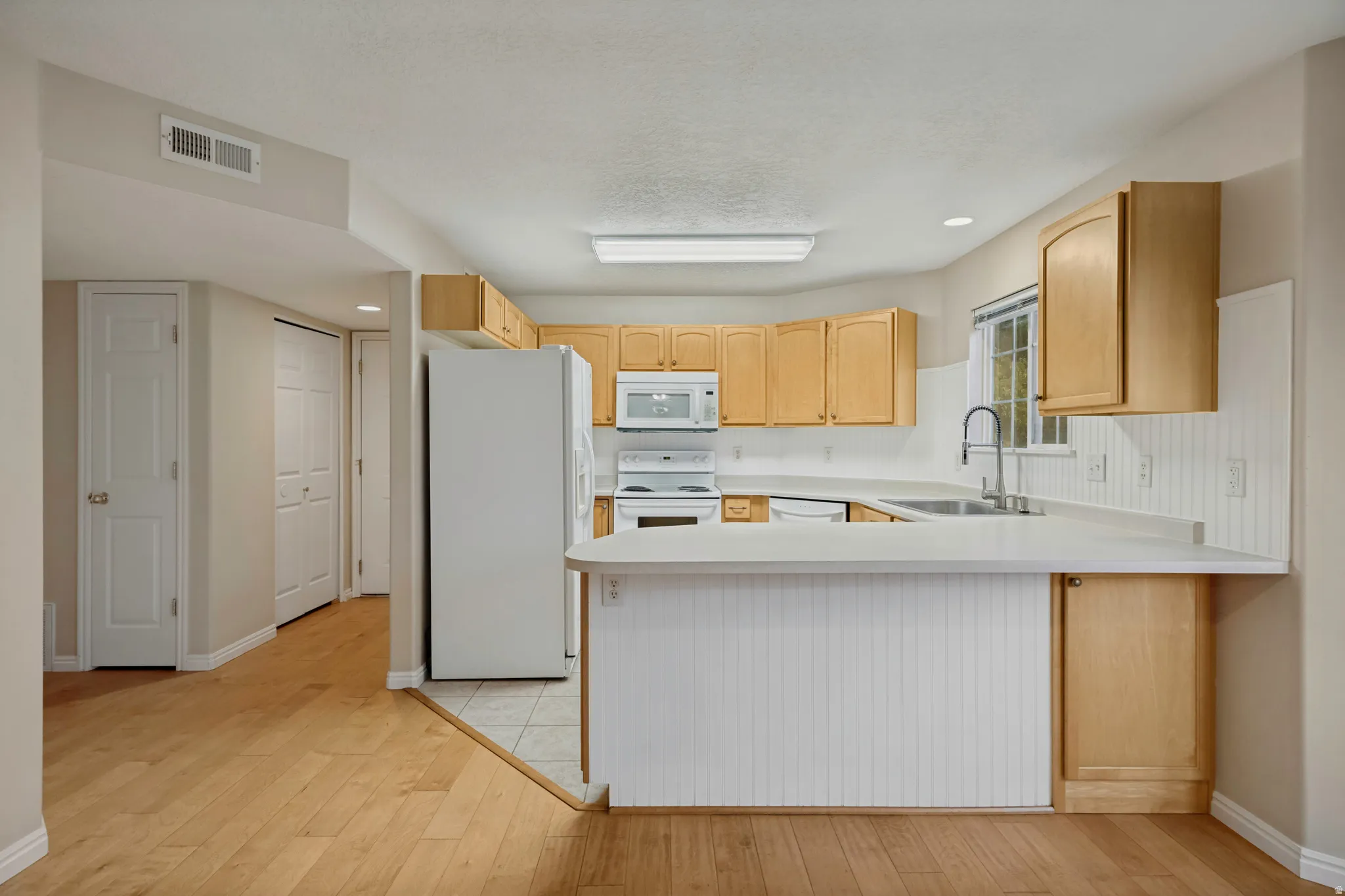 Kitchen featuring wood-finish cabinetry, white appliances, white countertops, and a stainless steel sink with a gooseneck faucet