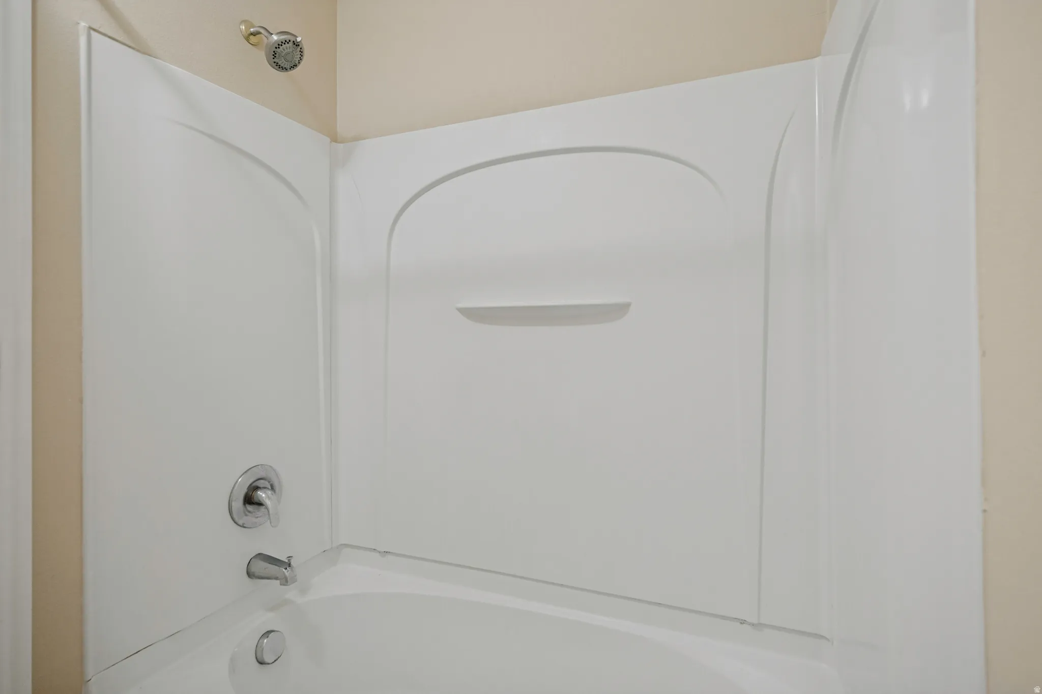 White fiberglass tub and shower combination with chrome fixtures and integrated shelving
