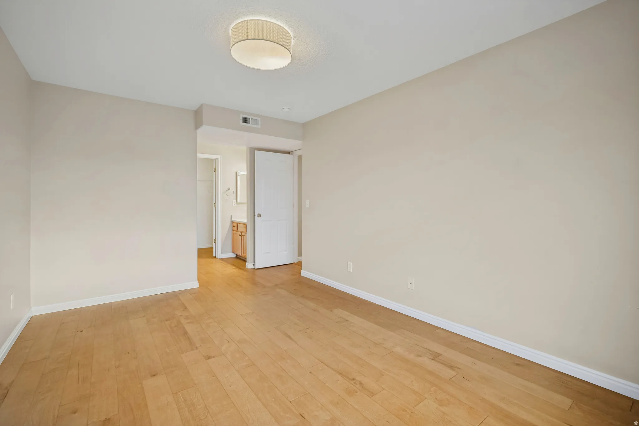 Light wood-finish flooring, neutral wall tones, recessed ceiling lighting, and a white paneled door
