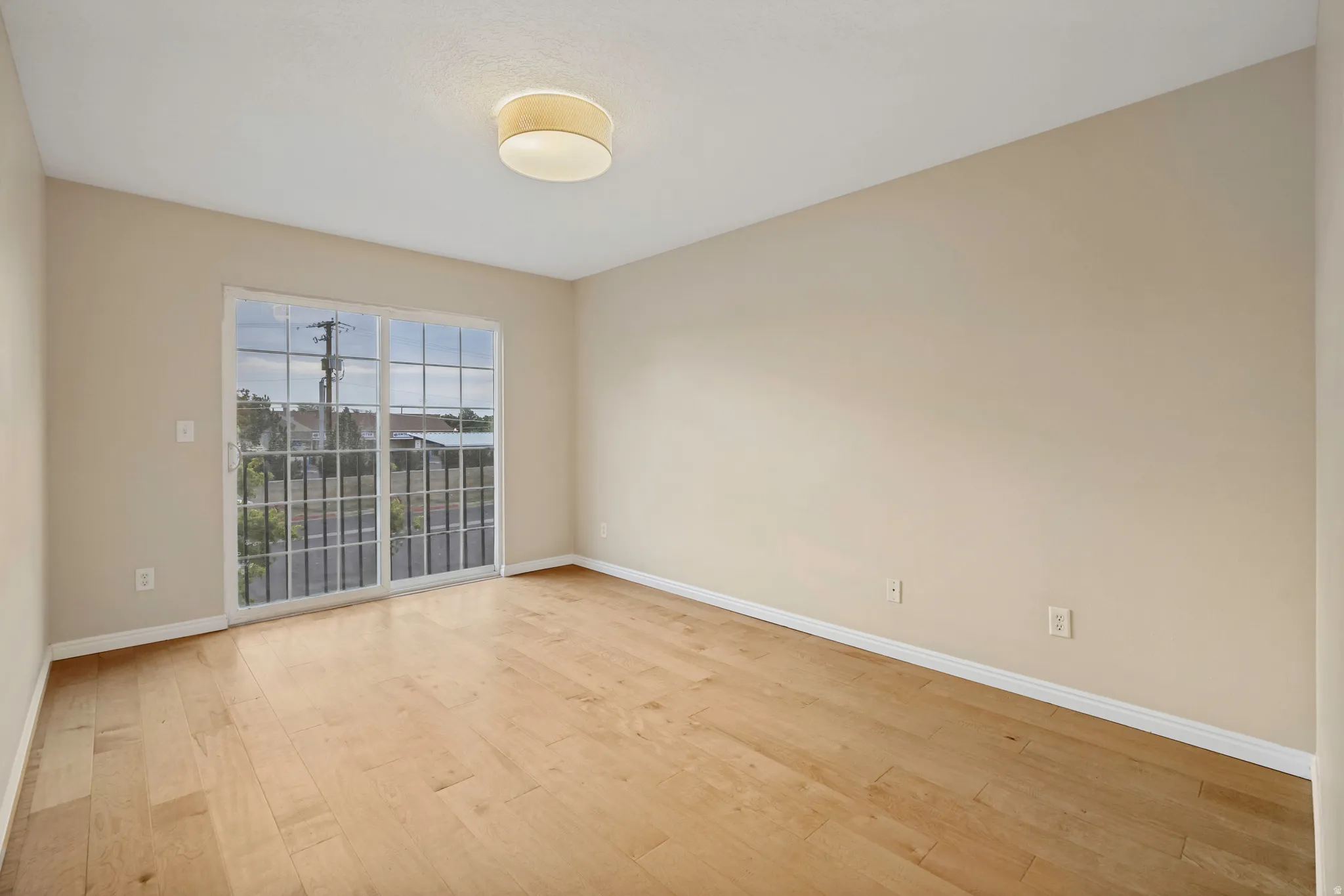Wood-finish flooring, sliding glass door with grids, neutral wall tones, and a ceiling-mounted light fixture