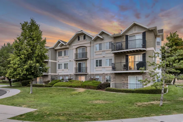 Multi-story building featuring stone and siding exterior, multiple private balconies with black railings, and a manicured lawn