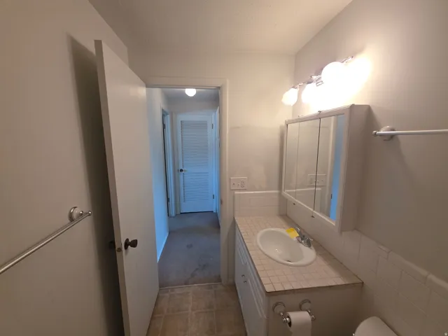 Recessed medicine cabinet with mirrored doors, vanity with integrated basin, tiled countertop, and wall-mounted lighting fixture