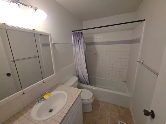 Recessed medicine cabinet, vanity with integrated sink, chrome faucet, tiled shower surround with accent band, and a white bathtub