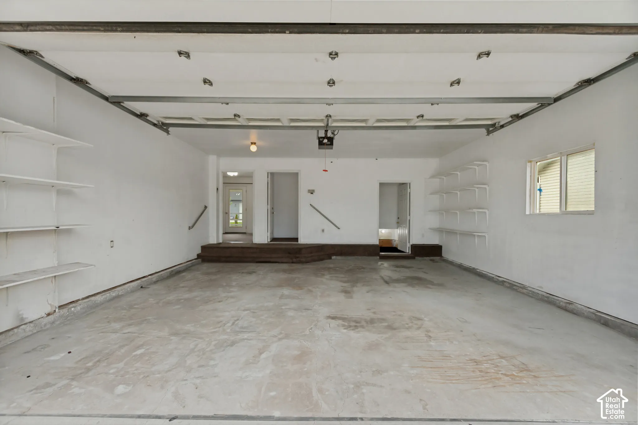 Spacious garage with a concrete floor, integrated shelving, and multiple access points