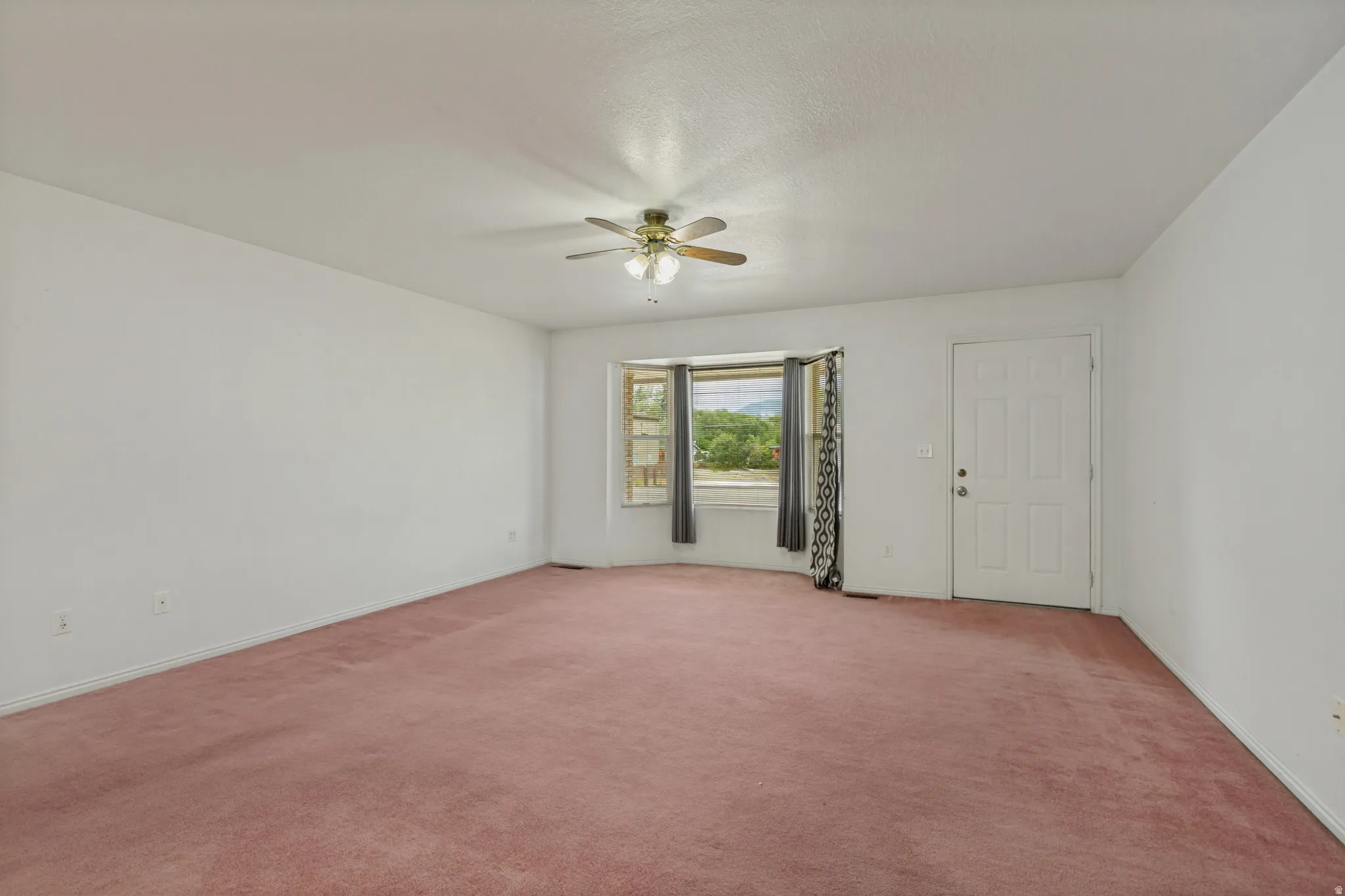 Recessed window bay, ceiling fan, white paneled entry door, and wall-to-wall carpeting