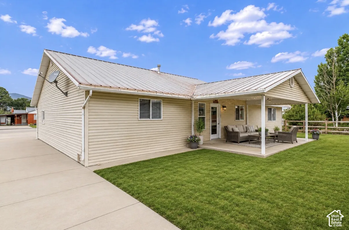 Expansive concrete patio with a covered section, mature lawn, and wood fencing