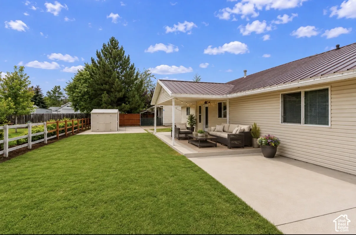 Expansive backyard with a manicured lawn, a white and wood fence, a spacious concrete patio, and a covered outdoor living area
