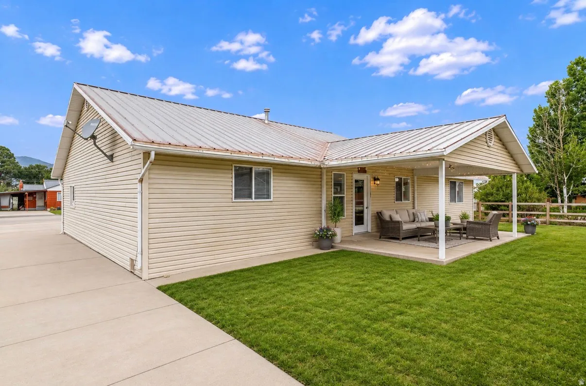 Expansive concrete patio with a covered section, mature lawn, and wood fencing