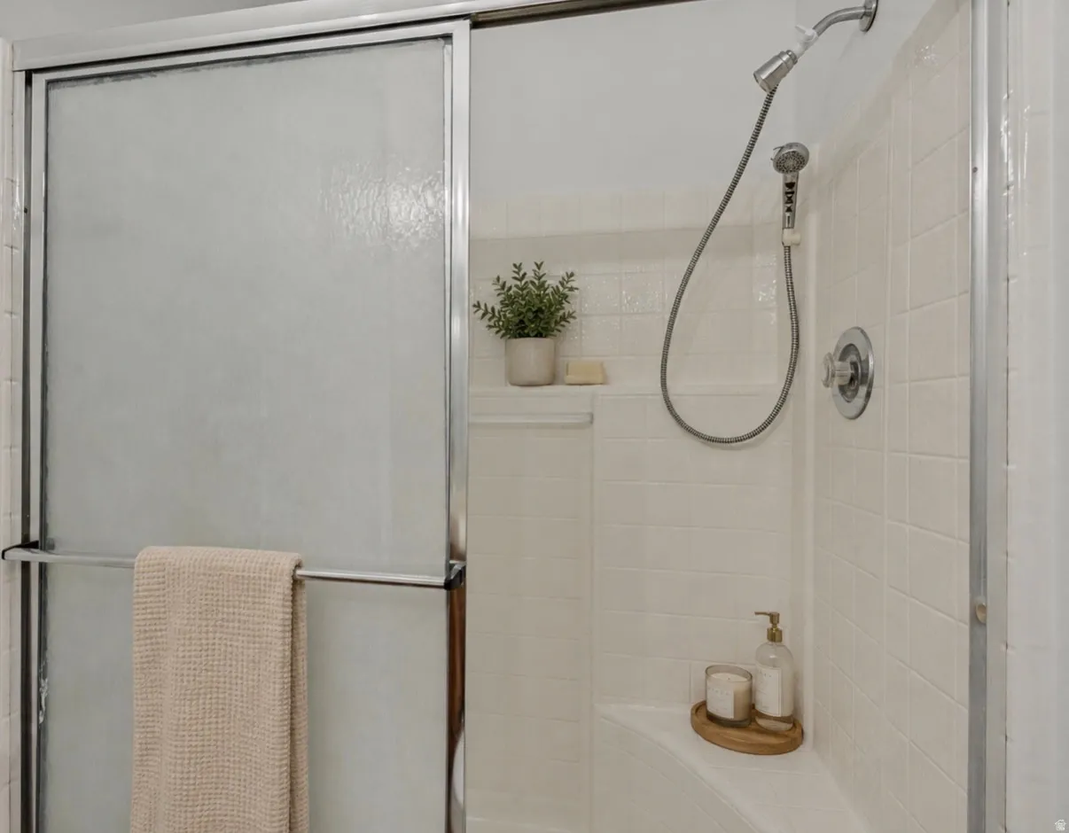 Primary bedroom shower. Shower enclosure featuring a sliding glass door, tiled walls, built-in shelving, and a shower head with an attached sprayer