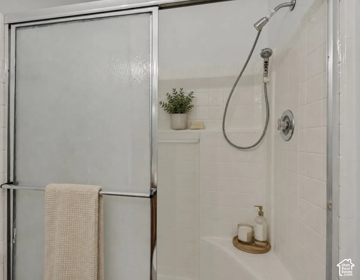 Primary bedroom shower. Shower enclosure featuring a sliding glass door, tiled walls, built-in shelving, and a shower head with an attached sprayer