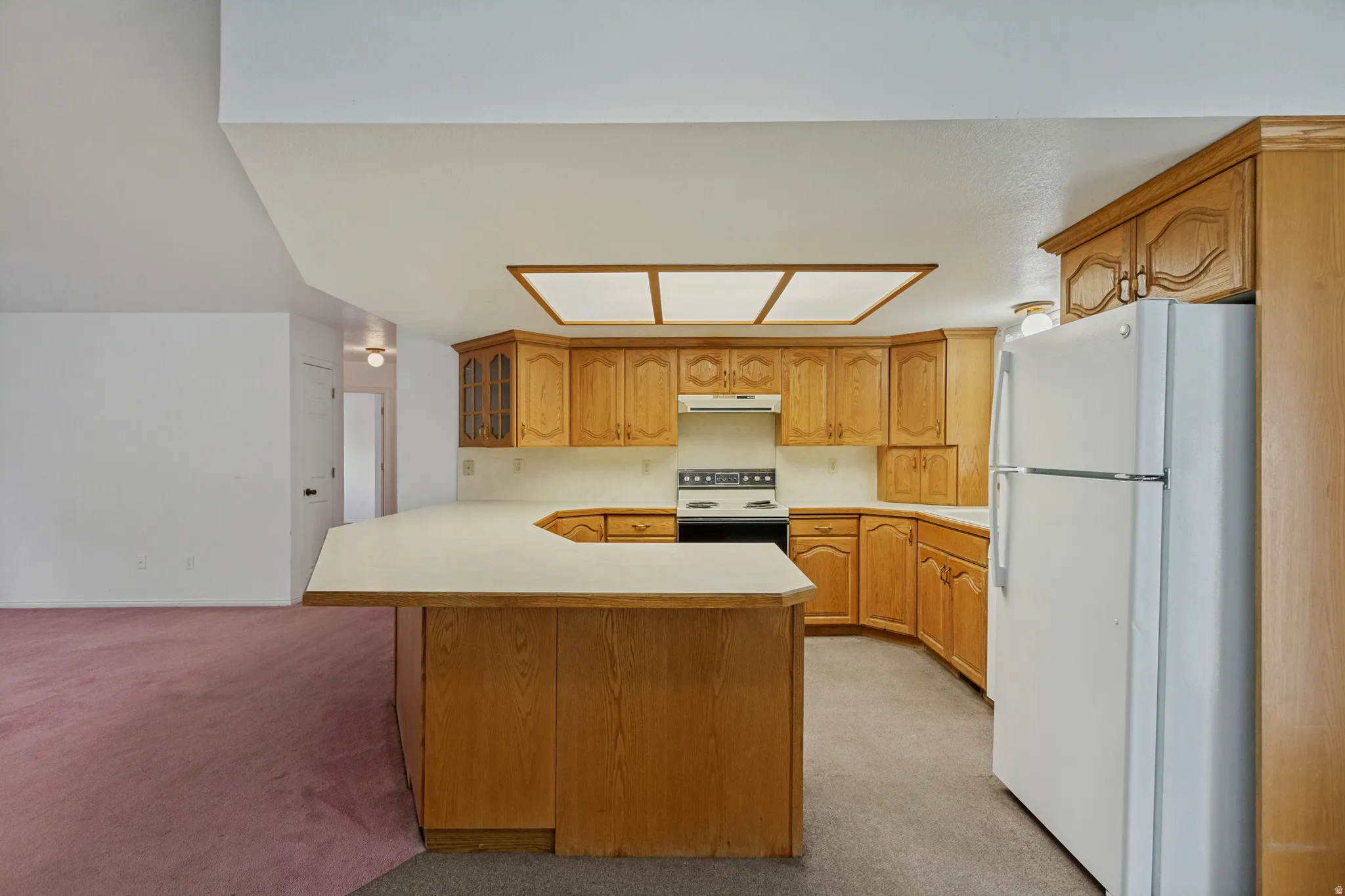 Kitchen featuring wood-finish cabinetry, white countertops, built-in range, and a breakfast bar