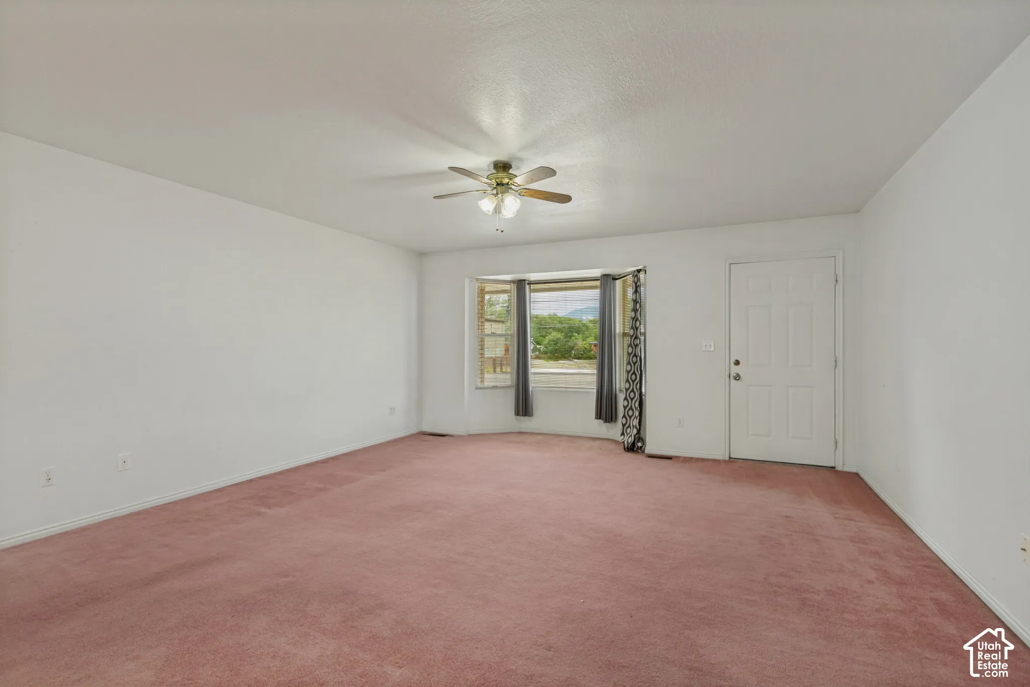 Recessed window bay, ceiling fan, white paneled entry door, and wall-to-wall carpeting