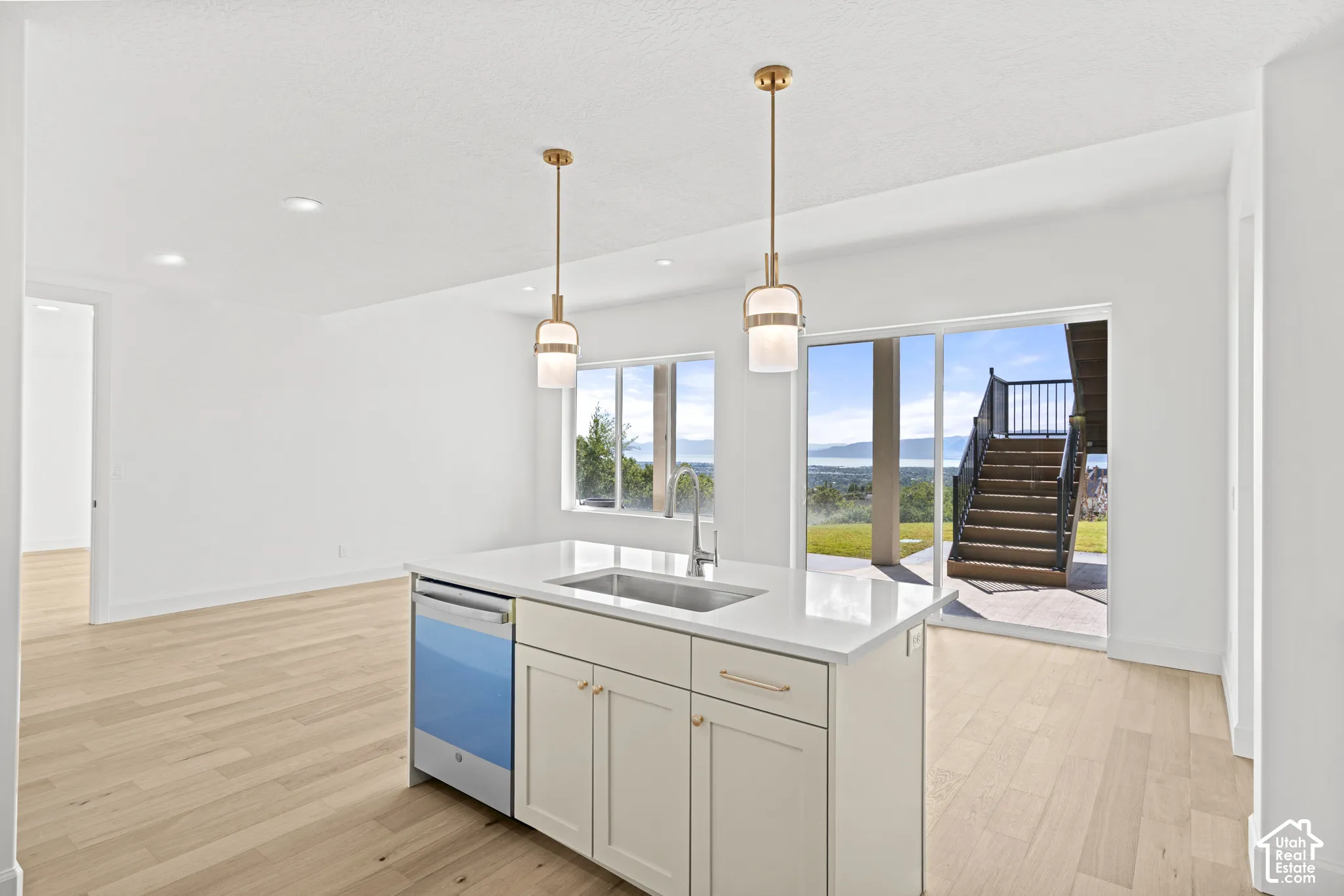 Kitchen island with integrated sink, white cabinetry, and stainless steel dishwasher